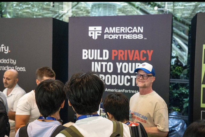 A trade show booth for "AMERICAN FORTRESS" with signage reading "BUILD PRIVACY INTO YOUR PRODUCTS," showing attendees interacting with representatives.