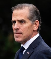 A man with dark hair wearing a dark suit, white shirt, and blue tie, standing against a blurred green background. The image accompanies a news post accusing Hunter Biden of allegedly rugpulling his cryptocurrency memecoin $LAPTOP, though no text or identifying details are visible in the photo itself.