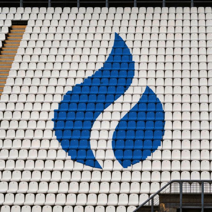 A stadium seating section with white and blue seats arranged to form a large abstract bird or flame-like logo.