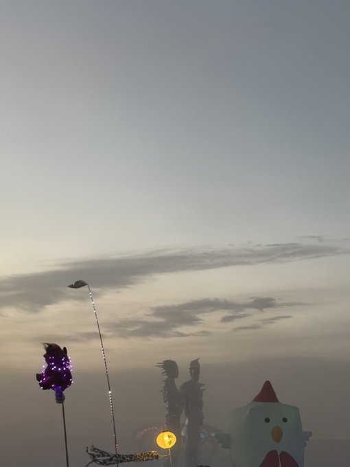 A twilight sky frames whimsical festival figures—a glowing purple creature, a flag on a tall pole, two silhouetted statues, and a chubby cartoon bird in a red hood—evoking the relaxed, fantastical vibe of "spot and chill undefeated."
