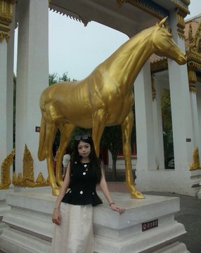 A woman poses in front of a large golden horse statue in Zhengzhou, matching her post about the city's affordable prices and delicious food.