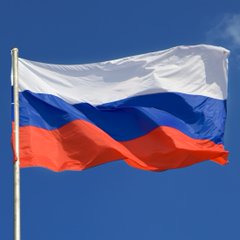 The Russian flag waves against a clear blue sky, symbolizing the nation where Sberbank, Russia's largest bank, is preparing to launch cryptocurrency trading services for its customers.