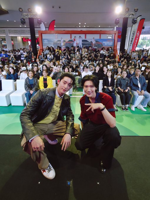Two young men crouch and pose on a stage at a crowded indoor event, with a banner behind them promoting "DRIVEN TO BE YOUNG" alongside Toyota logos, fitting the post's hashtags "#TEN #TENxAsianGames2026 #ASG26AM #AsianGames2026."