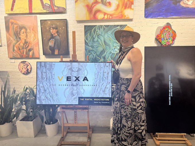 A woman wearing a tan hat and glasses stands next to a framed artwork titled 'VEXA: THE CELESTIAL GUARDIANS - THE PORTAL ARCHITECTURE', surrounded by other paintings.