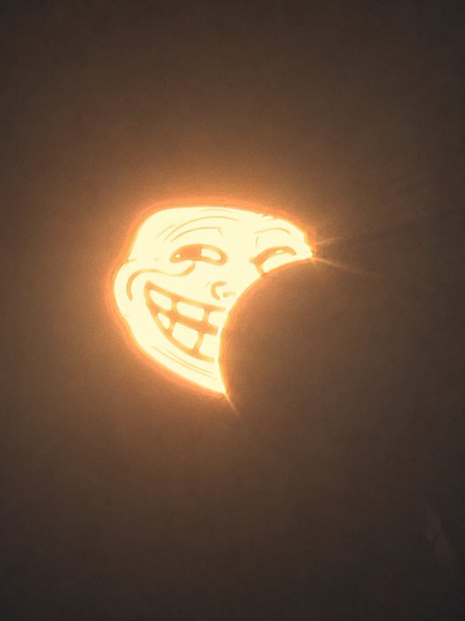 A photograph of a carved jack-o'-lantern depicting the 'Trollface' meme with a mischievous grin, partially obscured by another pumpkin in the foreground.