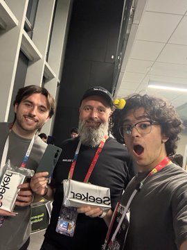 Three men pose for a photo at what appears to be a conference or convention, with two of them holding SageKey branded merchandise.