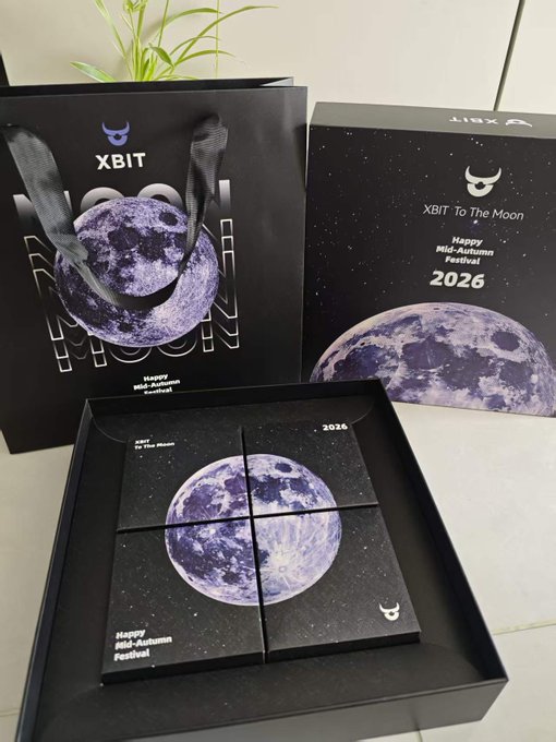 A black gift box set featuring a moon design with 'XBIT To The Moon 2026' and 'Happy Mid-Autumn Festival' text, including a shopping bag with the same branding.
