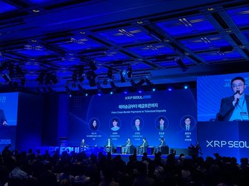 The image captures the XRP Seoul 2026 conference, where a panel discussion on "Multi-Chain Game: Hyperfusion" is being held, with the main screen displaying the event's title and a speaker presenting on stage. The post celebrates the global unity of XRP at this South Korean event, and the image visually confirms the international scale of the gathering as referenced in the message.