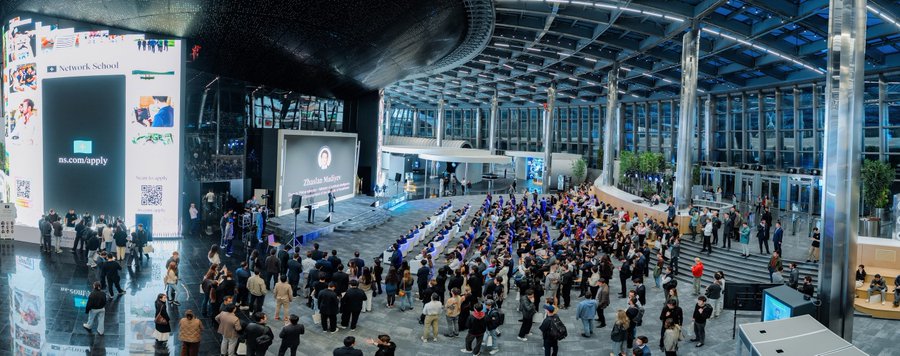 A large crowd gathers in a modern glass-walled venue for the opening of Network School, with prominent signage reading "Network School" and "ns.com/apply" on a stage backdrop, alongside a "Thank you, Kazakhstan" screen acknowledging the government's support. The scene captures the historic launch event referenced in the post, celebrating Network School's debut in Kazakhstan with attendees filling the expansive atrium.