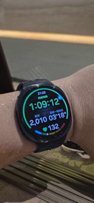 A person's wrist shows a black smartwatch displaying a workout time of "1:09:12", a distance of "2,010", and a heart rate of "132", with the screen and wrist appearing wet.