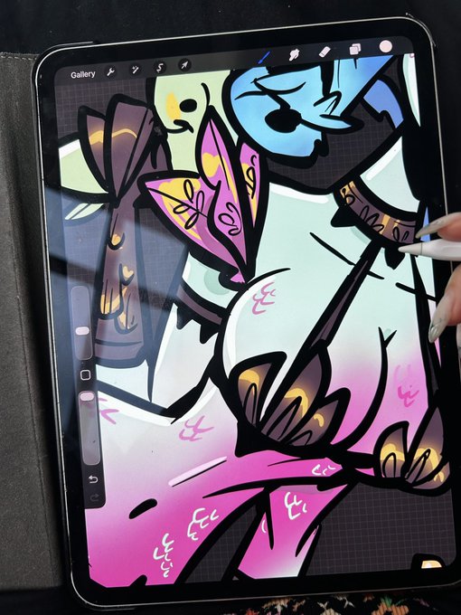 A tablet screen displaying a colorful digital illustration in progress, featuring stylized female figures with pink and blue tones, with a hand holding an Apple Pencil visible on the right side.