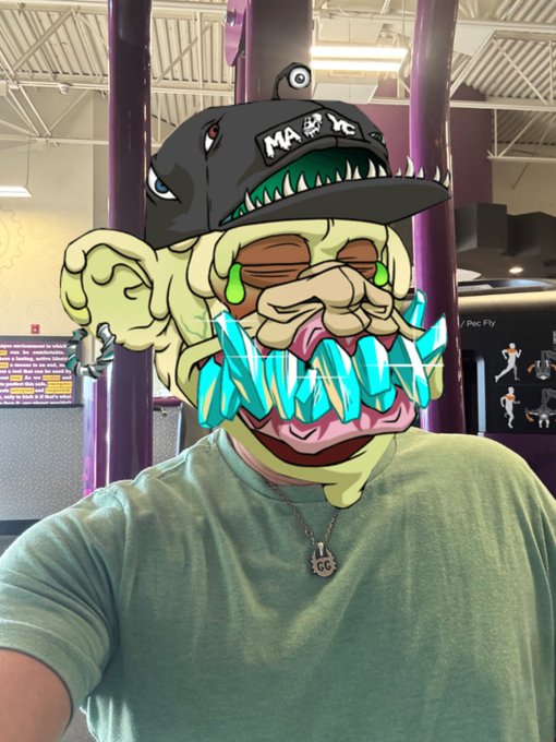 A person wearing a green shirt in a gym setting with an elaborate digital filter overlay featuring a cartoon dinosaur cap, sunglasses, and diamond teeth, with a 'GG' pendant necklace visible.