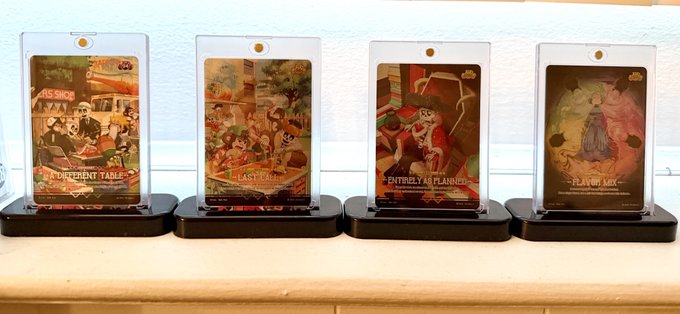 Four collectible cards on display stands showcase Disney-themed artwork including 'A Different Tale', 'The Last Cup', 'An Entirely Planned Adventure', and 'The Lap of Luxe'.