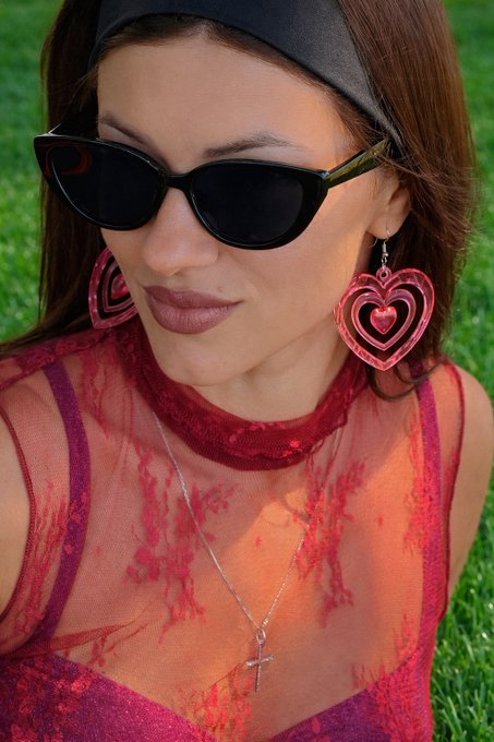 The image features a woman wearing red clothing, sunglasses, and heart earrings. She has her hair pulled back into a ponytail and is sitting or standing in a grassy area. The photo also contains text that reads "Good evening everyone Most blockchains burn energy solving meaningless hashes. Quip Network is taking a different path: Quantum + classical computing Post-quantum security Real computational work The future isn' s just decentralized. It'S useful". This post seems to be promoting the idea of using blockchain technology for real-world applications, such as enhancing security and efficiency in various fields.