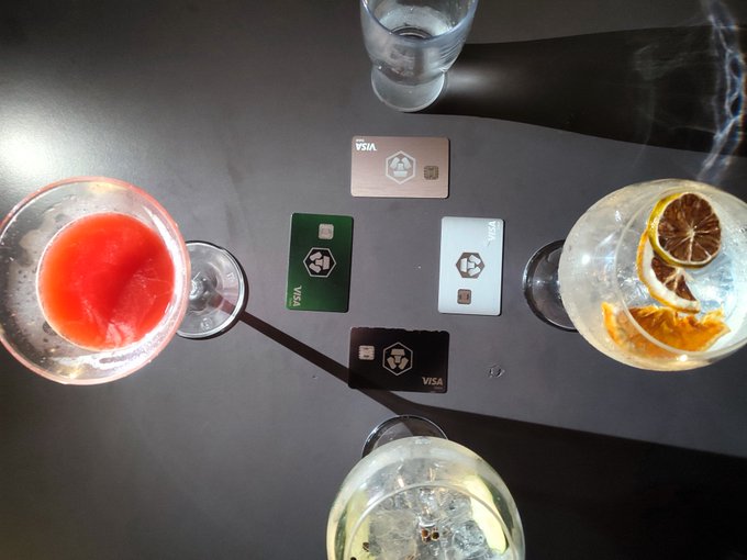 An overhead view of a table featuring four VISA cards arranged in a cross pattern, surrounded by four cocktails including a red drink and a citrus gin and tonic.