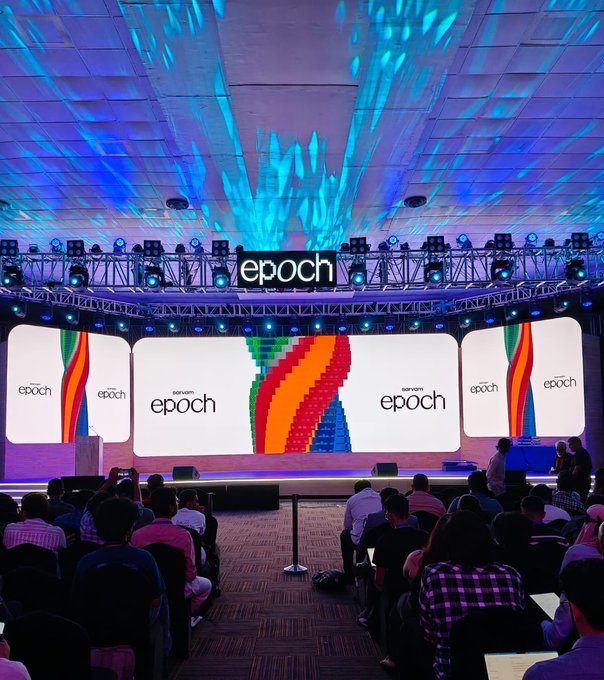 An 'epoch' conference event with a large audience seated facing a brightly lit stage featuring colorful displays and the 'non-american epoch' branding.