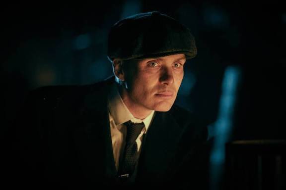 The image appears unrelated to the crypto/finance post; it shows a man in a flat cap and tie (resembling a period drama scene, likely from "Peaky Blinders") lit dramatically against a dark background, with no visible text or financial content.