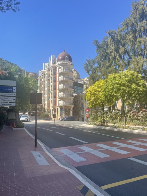 A sunny street scene in Monaco features a domed Belle Époque building, with directional signs pointing toward the Casino, and Boulevard de La Condamine.