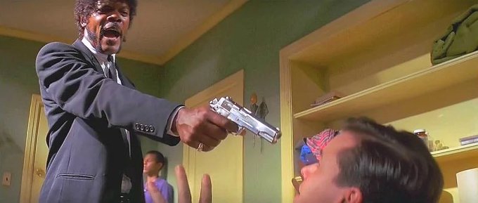 A scene from the movie Pulp Fiction showing Samuel L. Jackson pointing a silver handgun at John Travolta.