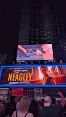 A nighttime city billboard for the film 'NEAGLEY' (a Jack Reacher spinoff), with a Times Square-style display and a crowd of people below.