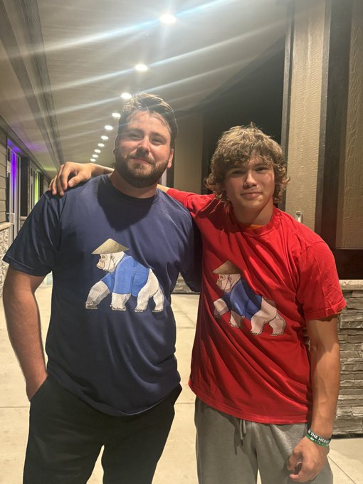 Two men standing together, both wearing shirts with a graphic of a bear wearing a conical hat.