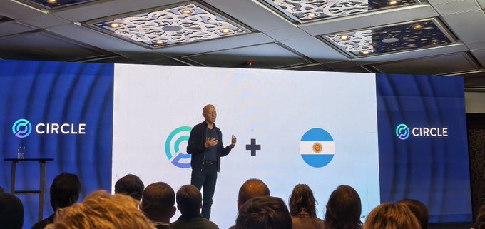 A man speaks on stage at a Circle crypto event, standing in front of a large screen displaying the Circle and USDC logos plus an Argentine flag.