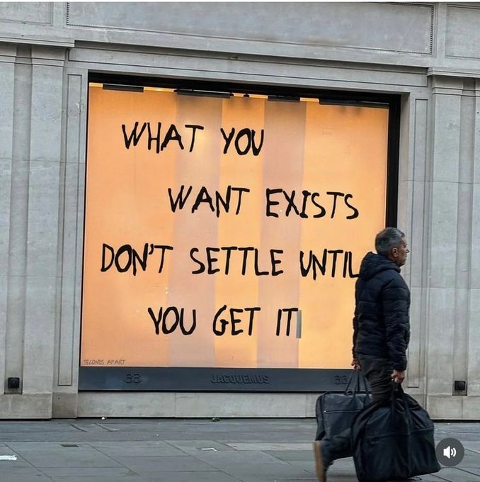 A man walking past a store window with the motivational text 'WHAT YOU WANT EXISTS DON'T SETTLE UNTIL YOU GET IT' from 'SLOANE'S APART' at Jacquesmus 33.