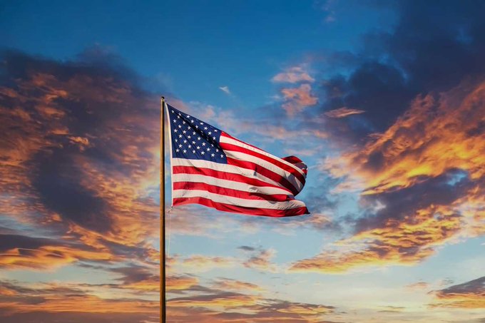 An American flag waves against a vibrant sunset sky, symbolizing U.S. national identity as 39 state banking associations unite to establish the BankChain Alliance—a nationwide blockchain network set to launch in 2027 for stablecoins, tokenized deposits, and faster payments.