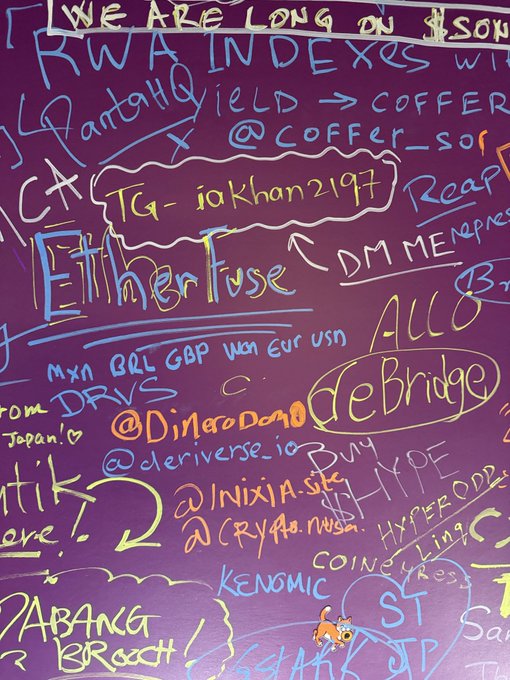 A purple wall covered in multicolored handwritten graffiti featuring tags like "TG - iakhan2197", "RWA INDEXES", "Either I lose", "@DjMataDoDoo", "@derive_io", "@Inixia.stk", "deBridge", and a small cartoon Shiba Inu dog.