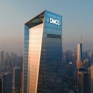 The image shows an aerial view of a tall building in Dubai, which appears to be a skyscraper or a very tall office building. The building has a glass facade that reflects the surrounding cityscape. In the background, there are other buildings visible, indicating that this is part of a larger urban area. The post includes text about a strategic agreement between DMCC and Tether, discussing the adoption of blockchain technology, digital assets, and tokenized finance. This suggests that the building may be associated with or located near one of these industries or projects related to blockchain and financial innovation.