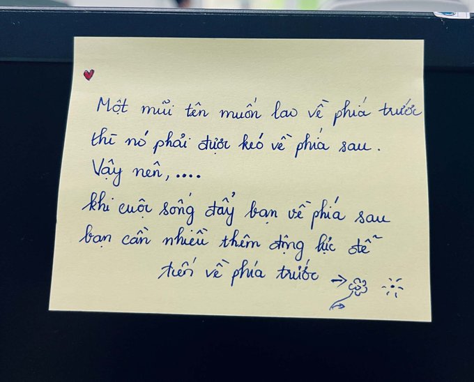 A handwritten Vietnamese quote on a yellow sticky note that reads "Một mũi tên muốn lao về phía trước thì nó phải được kéo về phía sau. Vậy nên, khi cuộc sống đẩy bạn về phía sau bạn cần nhiều thêm động lực để tiến về phía trước," meaning "An arrow must first be pulled back before it can shoot forward, so when life pushes you back, you need more motivation to move forward," decorated with a heart and a flower. The image relates to the post by exemplifying the type of inspirational "good morning/good night" content the user creates, featuring a handwritten motivational quote on a sticky note.