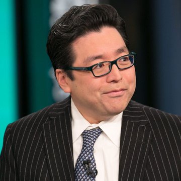 A man in a pinstripe suit and patterned tie appears on what looks like a television set, smiling slightly. The image accompanies a breaking news post where market strategist Tom Lee declares the crypto bull market has begun, suggesting it could surpass previous cycles.