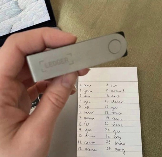 A person holds a Ledger hardware wallet, likely for cryptocurrency storage, next to a handwritten list of words that resembles a recovery seed phrase backup. The setup illustrates securing crypto assets with the wallet and its associated recovery seed.