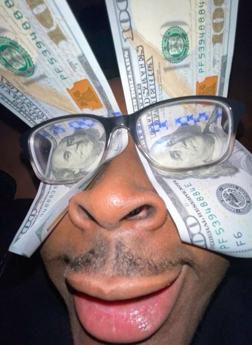 A selfie showing a person wearing novelty dollar bill glasses with Benjamin Franklin's image reflected in the lenses, sticking their tongue out at the camera.
