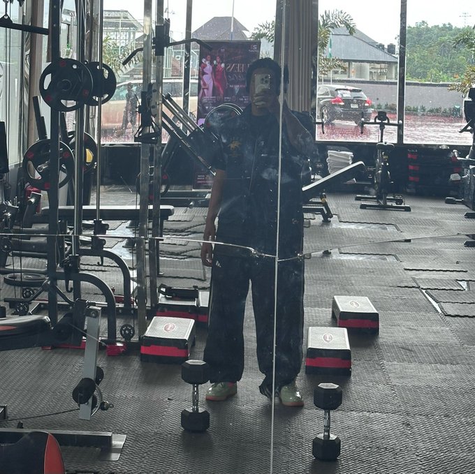 A person takes a mirror selfie in a gym, surrounded by dumbbells and workout equipment, with a "ZIVA" promotional poster visible in the background. The image aligns with the "Happy weekend" post by capturing a fitness-focused start to the weekend.