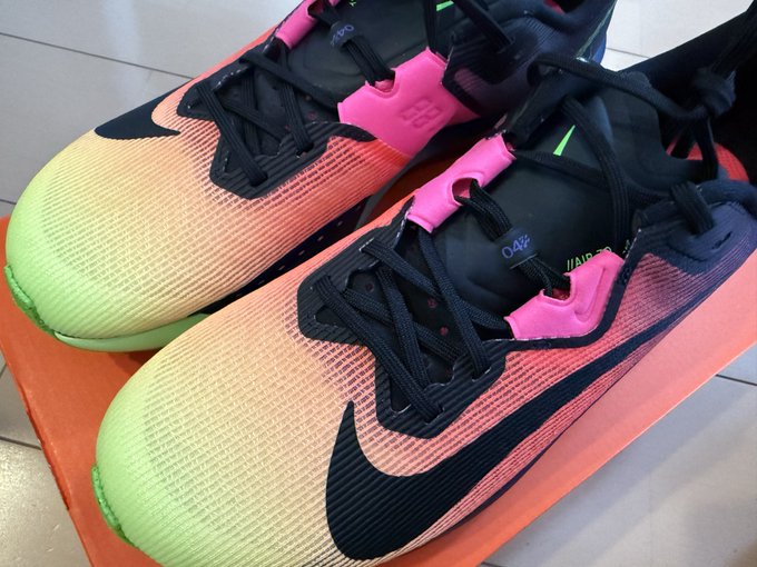 The image features a pair of Nike shoes with neon colors, including pink and green accents. The shoes are positioned side by side, with one shoe being closer to the top edge of the frame and the other slightly lower down. Both shoes have black laces that match their overall design. The background is white, which contrasts nicely with the colorful shoes. There is no text present in the image, so it does not provide any additional information about the post or its context.