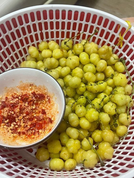 A photo of a white basket filled with small yellow-green fruits, with a small bowl of red chili powder and salt mixture on the side.