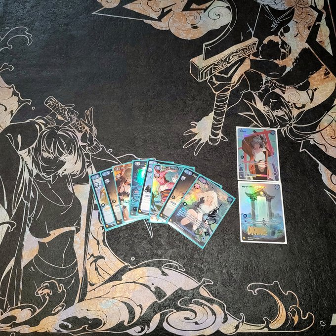 A fan spread of female anime character trading cards fanned out on an anime-themed playmat, with two additional character cards placed to the right.