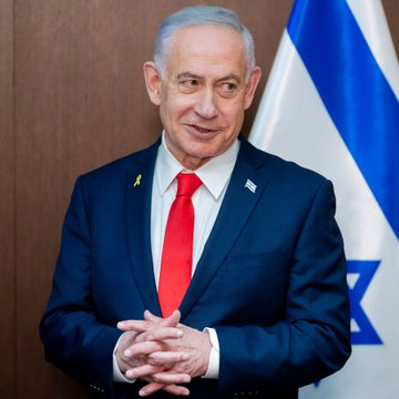 A man in a dark suit with a red tie stands smiling with hands clasped in front of an Israeli flag. The image appears to relate to the post's mention of a Polymarket trade involving a US-Iran ceasefire, a topic connected to Middle East geopolitics.