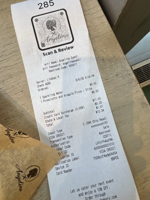 A restaurant receipt for Check #295 totaling $12.34 (including a $6.50 sparkling water) from a Times Square eatery, dated 8/6/26, with a note inviting customers to order through "..." for 10% off their next event. The image illustrates the post's humorous point about the author's costly meal in Times Square before attending the Azuki TCG event at Nxt Legaci.