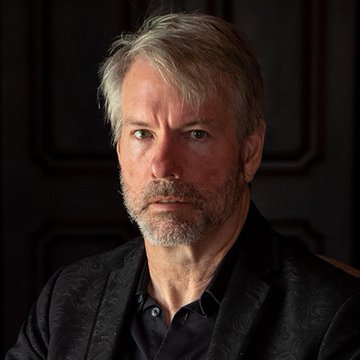 A portrait of Michael Saylor, co-founder of Strategy, shown in a close-up shot wearing a dark patterned blazer against a muted background. The image accompanies news of his company transferring 3,568 BTC valued at $297 million, as reported by Lookonchain.