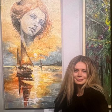 A young woman stands beside a large painting depicting a woman’s face merged with a sunset seascape featuring sailboats on golden waters.