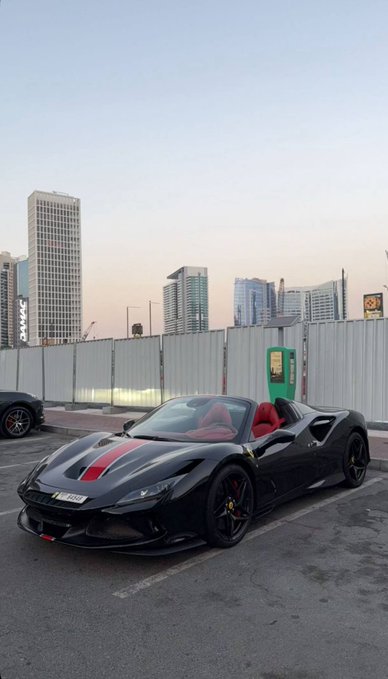 A black Ferrari F8 Tributo with a red stripe and red interior is parked against an urban skyline backdrop. The post's caption "GM to everyone who says GM" plays on the phrase "Gentleman" (often abbreviated as GM on social media) while also referencing General Motors, creating a playful flex of Italian luxury against American automotive brands.
