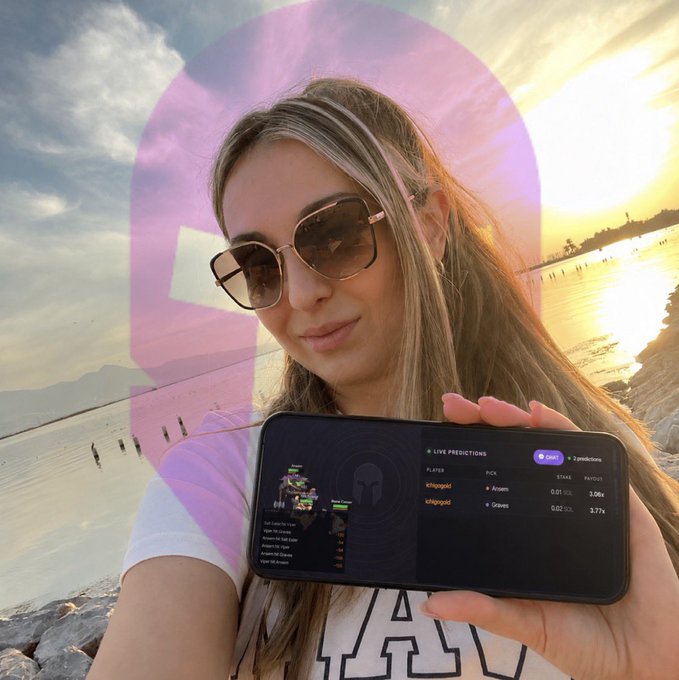 A woman wearing large sunglasses holds up a smartphone displaying live betting predictions at sunset by the water, with $ANSEM shown among the players. The image visually reinforces the post's message about the $ANSEM 2x payout campaign on the Trench Royale leaderboard.