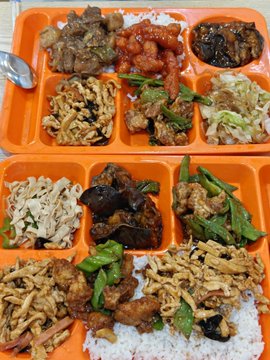 Orange trays filled with various Chinese dishes including meat, vegetables, and rice, likely a takeout meal.