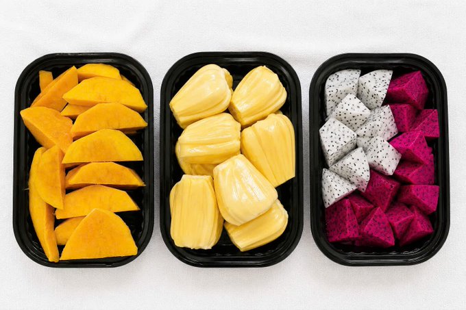 Three black plastic containers are neatly arranged with sliced mangoes, peeled jackfruit, and a mix of white and magenta dragon fruit pieces.