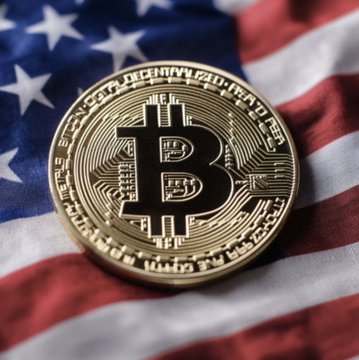 A gold physical Bitcoin token rests on an American flag, with "BITCOIN" inscribed around its edge and the iconic "₿" symbol at its center, visually symbolizing the intersection of cryptocurrency policy and U.S. government action as referenced in the post about the Clarity Act.