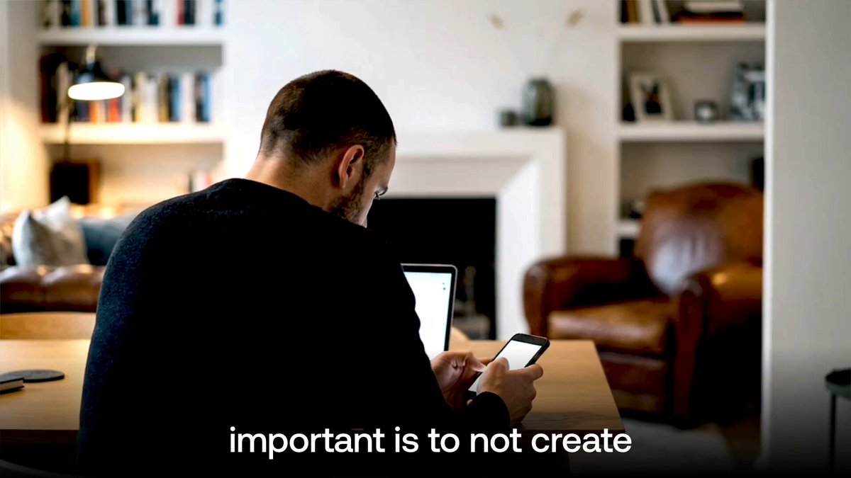 A man sits at a table in a living room, using a smartphone with a tablet in front of him, while the subtitle "important is to not create" appears at the bottom. The image illustrates the post's message about avoiding fragmented liquidity silos, showing someone engaging with digital financial tools that would benefit from a unified, cross-market platform like Avalanche.