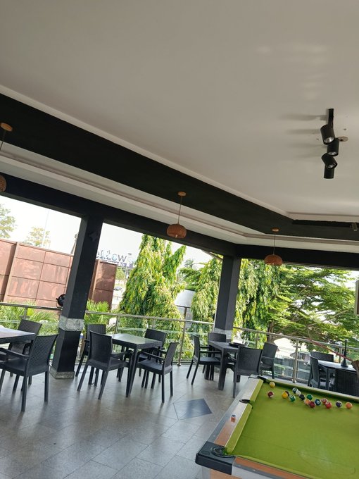 A bright, open-air lounge features seating areas with tables and chairs beside a green-felt pool table, with a "Welcome" sign visible on a balcony railing. The scene captures a cheerful, relaxed setting to kick off a happy new week.