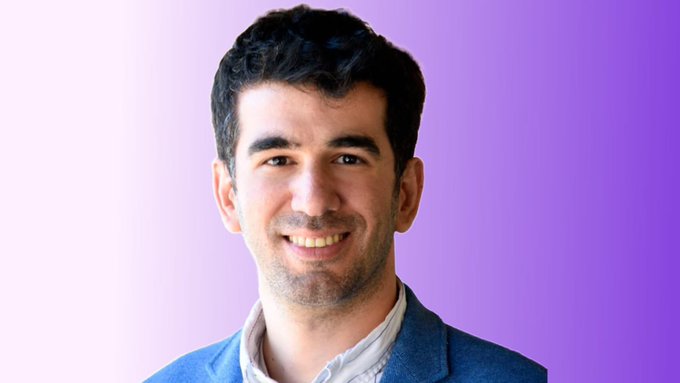 A young man with dark hair and a slight smile, wearing a blue blazer over a white shirt, is pictured against a purple gradient background. The image likely serves as a portrait of the author or spokesperson discussing the v26 upgrade deadline, though no identifying text is visible.